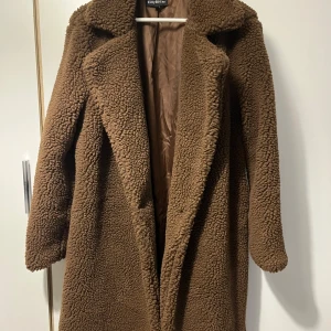 Brun teddykappa - Säljer en underbar brun teddyjacka från EillyBazar i storlek L. Jackan har en oversized look, bred krage. Materialet är mjukt och fluffigt, perfekt för kalla dagar. Fodrad insida för extra komfort och värme. Lång kappa (ungefär 1,2 m). Med dubbla knappar. Passar kalla vintrar och höst som ger en super mjuk och skön känsel. 🍁✨  UTAN en enda användning! Bara fattas prislapp.  Hör av er om frågor ❤️  Vänligen,