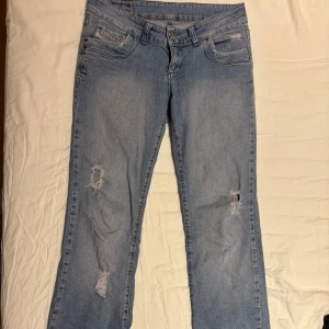 Ljusblå slitna jeans från Diesel - Ljusblå jeans från Diesel med slitningar på benen och bakfickorna. Klassisk femficksmodell med dubbla knappar i midjan och utsvängda ben. Jeansen har en avslappnad vibe och är tillverkade i mjukt bomullsjeans. Perfekta för dig som gillar en casual och trendig look.