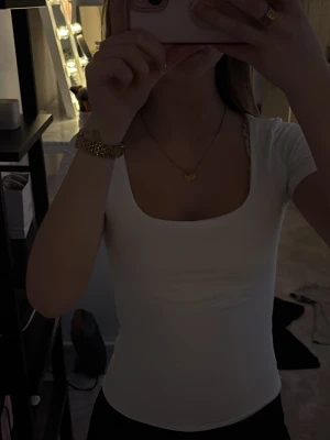 Vit  topp med fyrkantig ringning - Säljer en enkel och stilren vit topp med korta ärmar och fyrkantig ringning. Toppen har en tight passform som framhäver figuren. Perfekt att matcha med jeans eller kjol för en clean look.
