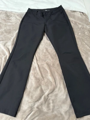 VERA FAIRE KOSTYMBYXA - Snygga svarta kostymbyxor med klassisk rak passform och hällor för skärp. Byxorna har diskreta fickor fram och bak, samt en stilren look som passar till många olika stilar. Perfekta för dig som vill ha en clean och tidlös vibe.