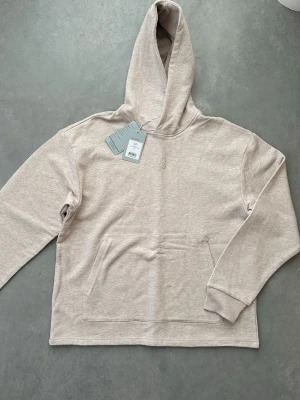 Ljusgrå hoodie från Amendi - Säljer en stilren ljusgrå hoodie från Amendi i mjuk bomullsblandning. Hoodien har en stor huva, broderad logga på bröstet och en klassisk känguruficka framtill. Perfekt för en avslappnad och clean look. Köpt några månader sedan. Inte använd