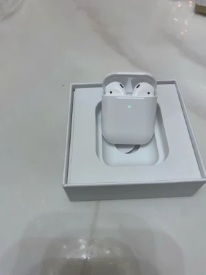 Apple AirPods med laddningsetui - Säljer ett par vita Apple AirPods med laddningsetui. Trådlösa in-ear-hörlurar i stilren design, tillverkade i blank plast. Kompatibla med iOS-enheter och levereras i originalförpackning. Perfekta för musik, samtal och vardagsbruk.