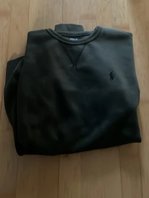 Polo Ralph Lauren - Snygg mörkgrön sweatshirt från Polo Ralph Lauren med klassisk rund halsringning och svart diskret broderad logga på bröstet. Tröjan har en relaxed fit och är tillverkad i mjukt material som passar perfekt till jeans eller joggers. Storlek M men passar också S. Tröjan är i nyskick och har knappt används. Skriv för fler bilder, frågor. Pris kan diskuteras. 
