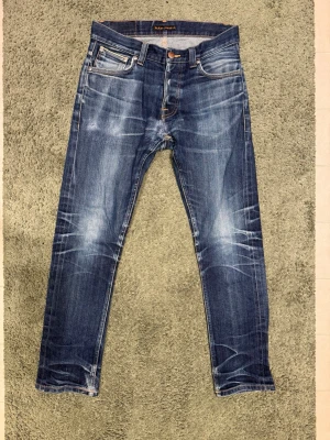 Nudie Jeans Grim Tim Dry Deep Selvage - Säljer dessa asfeta selvage jeans från Nudie jeans. Modellen är grim Tim och de är i färgen dry deep selvage. Storlek W29 L30. De har sjuka fades såsom whiskers och honeycombs. De har dessutom fades från mobil och knappar. De har blivit reparerade i fickan, längst ned vid benet, i grenen och knappen högst upp har bytts ut till en ny. De är helt nytvättade då de nyss blivit reparerade så kommer att stretchas ut igen efter användning. Säljer på grund av att jag köpt ett par nya att bryta in. 🙌