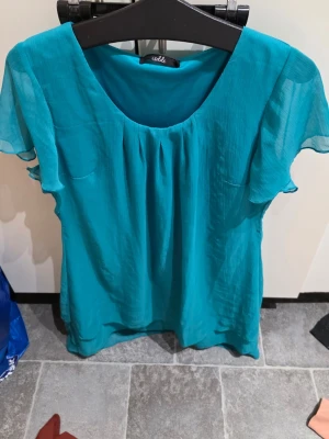 Turkos klänning  från Isolde - Turkos klänning Isolde med korta, luftiga ärmar och rund halsringning. Tillverkad i ett lätt, transparent tyg som ger ett flowy intryck. Perfekt för dig som gillar färg och vill ha en bekväm men snygg look.