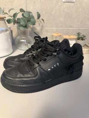 Svarta Nike N.354 sneakers - Säljer ett par svarta Nike N.354 sneakers i läder med klassisk låg profil och svarta skosnören. Snygg detalj med vit N.354-text på sidan och diskret Nike-logga. Perforerad tå för extra ventilation och bekväm passform.