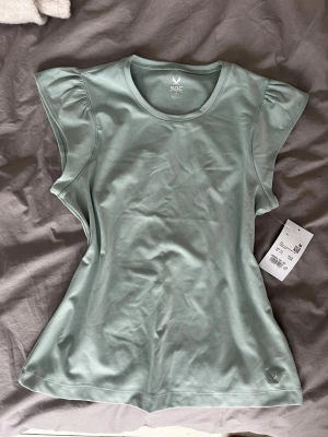 Ljusgrön träningstopp från SOC - Sportig ljusgrön topp från SOC med rund halsringning och korta volangärmar. Tillverkad i ett mjukt och stretchigt syntetmaterial som passar perfekt för träning. Enkel och stilren design utan mönster eller tryck.