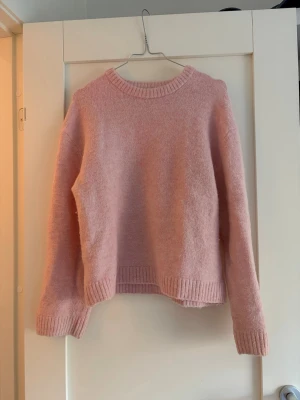 Ljusrosa stickad tröja - Mysig ljusrosa stickad tröja med rund halsringning och ribbade muddar vid ärmslut och nederkant. Tröjan har en rak och är perfekt för att hålla värmen under kyliga dagar.