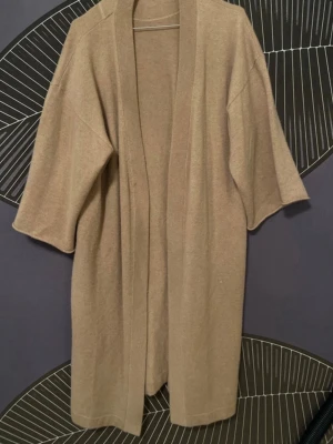 Beige kofta från Filippa K Soft Sport - Säljer en beige, öppen kofta från Filippa K Soft. Koftan har en avslappnad passform med vida trekvartsärmar och är tillverkad i Kashmir material. Perfekt att slänga på sig över en t-shirt eller topp.