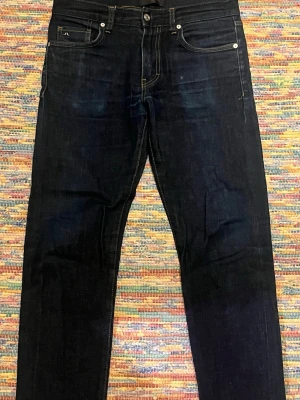 Mörkblå jeans från J.Lindeberg - Snygga mörkblå jeans från J.Lindeberg med klassisk femficksmodell och kontrastsömmar i gult. Jeansen har rak passform och är tillverkade i ett slitstarkt denimtyg. Perfekta för en stilren och enkel look.