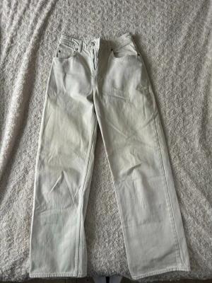 Vita raka jeans med hög midja - Säljer ett par vita jeans med raka ben och hög midja. Klassisk femficksmodell med bälteshällor och dragkedja. Perfekta för en clean och stilren look. Materialet är kraftig denim i bomull.