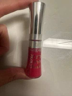 L'Oréal Glam Shine Blush läppglans - Läppglans från L'Oréal Paris i serien Glam Shine Blush. Färgen är en intensiv rosa med glansig finish. Förpackningen är smal med silvrigt lock och genomskinlig nedre del som visar färgen. Perfekt för dig som vill ha glansiga och färgstarka läppar.