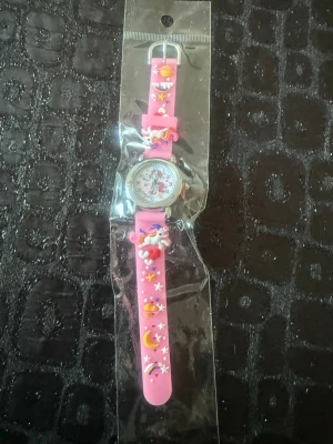 Rosa enhörningsklocka med stjärnor - Supergullig rosa klocka med enhörning, planeter, månar och stjärnor på armbandet. Klockan har ett färgglatt motiv och armbandet är gjort i mjuk syntet. Perfekt accessoar för dig som älskar magiska detaljer och färg. Kommer från ett djur och rökfritt hem. 