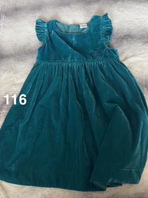 Petrolblå sammetsklänning med volangärm - Säljer en söt petrolblå klänning i mjuk sammet med glittriga detaljer. Klänningen har volangärmar och rund halsringning, samt ett lätt utställt kjolparti. Perfekt för dig som gillar en elegant men lekfull stil.🌸 Fint använt skick. Storlek 116. 