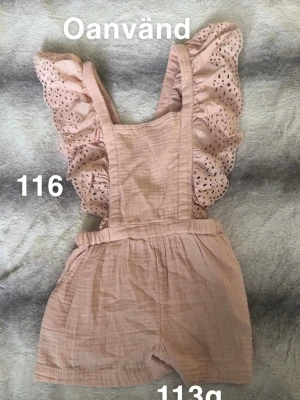 Ljusrosa byxdress med volangärmar - Supersöt ljusrosa byxdress med volangärmar och broderade detaljer. Byxdressen har resår i midjan och korta ben, perfekt för en trendig och bekväm look. Tillverkad i mjukt, luftigt tyg som känns skönt mot huden.🌸 Oanvänd. Storlek 116