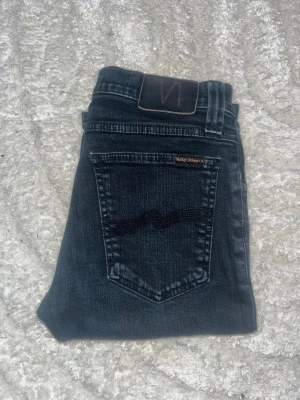 Nudie jeans - Snygga mörka jeans från Nudie Jeans, modell tight long John. Midja 34cm, längd 101cm. JAG SKICKAR EJ FLER BILDER NÄR JAG BÄR JEANSEN! för bättre inblick i passformen rekommenderar jag att googla på modellnamnet. För storleksguide kolla måtten noggrant då jeansen alltid kan vara uppsydda heller krympta och jag ej tar emot returer :) s6,4
