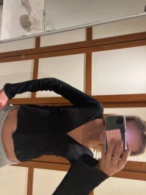 Svart topp med knytband - Snygg svart topp med långa ärmar som går ut i slutet och knytband i midjan. Toppen har en djup v-ringning, vilket ger en trendig och ungdomlig look. Perfekt att styla med både jeans och kjol.