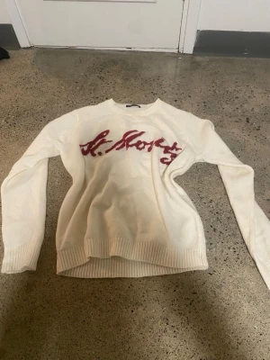 Vit stickad tröja Brandy Melville - Vit stickad tröja från Brandy Melville med röd text. Tröjan har rund halsringning, långa ärmar och ribbade muddar vid ärmslut och nederkant. Perfekt för dig som gillar en avslappnad och trendig look.