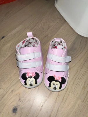 Rosa babyskor med Minnie Mouse LC Waikiki Skor, Rosa, EUR 20 - Säljer ett par söta rosa babyskor med Minnie Mouse-motiv framtill och vita kardborreband. Skorna har en liten rosa rosett och mönstrat innerfoder med Disney-figurer. Perfekta för små barn som gillar Disney och vill ha något gulligt på fötterna.