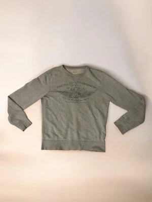 Tröja från polo Ralph Lauren  - Säljer en grå sweatshirt från Denim & Supply med tryck framtill. Tröjan har rund halsringning, långa ärmar och ribbade muddar vid ärmslut och nederkant. Perfekt till jeans och enkel att matcha med andra plagg.