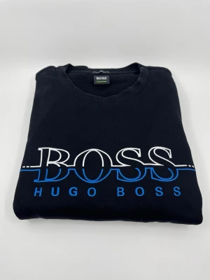 Svart Hugo boss tröja - Svart tröja från Hugo Boss i slim fit med stor vit woch klassisk BOSS- logga på bröstet. Perfekt för dig som gillar stilrena och klassiska designer med en modern touch. Tröjan har använts ett fåtal gånger med varsamhet men är nästan helt ny. Hör av er vid frågor!😇 Pris kan diskuteras! Skriv om mer bilder!