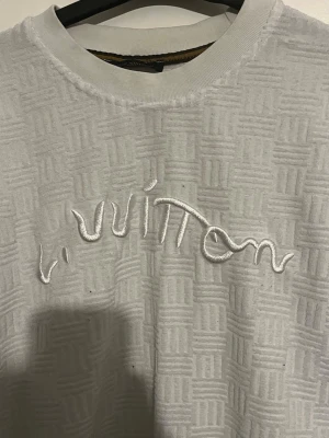 Vit Louis Vuitton sweatshirt - Exklusiv vit sweatshirt från Louis Vuitton med upphöjt rutmönster i tyget och broderad logga framtill. Tröjan har rund halsringning och ribbade muddar. Perfekt för dig som vill ha en stilren och lyxig look. Storek M OBS ÄKTA IFRÅN FRANKRIKE PRISLAPP KAN VISAS 