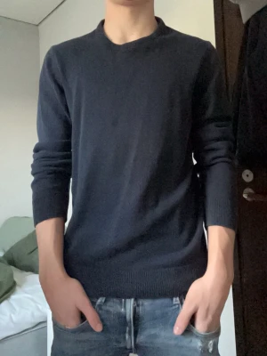 Mörkblå rundhalsad tröja - En stilren mörkblå tröja med rund halsringning och långa ärmar. Tröjan har ribbade muddar vid ärmslut och nederkant, vilket ger en snygg passform. Perfekt för lager-på-lager och enkel att matcha med jeans eller chinos.