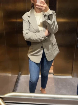 Beige kavaj med klassisk passform - Stilren beige kavaj med två knappar framtill och klassiska slag. Rak modell som ger en snygg siluett, perfekt att matcha med jeans eller kostymbyxor. Materialet ser ut att vara en mjuk bomulls- eller polyestermix. Inga synliga loggor eller märken.