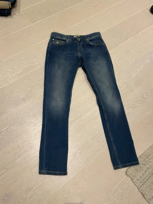 Morris  jeans - Snygga blå slim fit jeans från Morris med klassisk femficksdesign och gul kontrastsöm. Jeansen har en lätt tvättad look med slitningar på låren och knäna. Perfekta för en trendig och avslappnad stil.