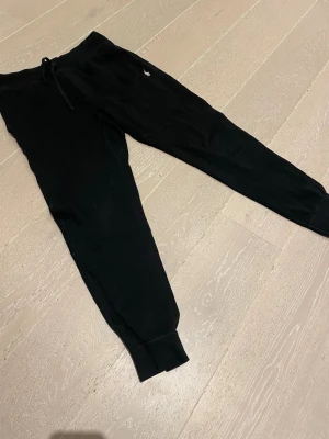 Svarta mjukisbyxor Polo Ralph Lauren - Svarta mjukisbyxor från Polo Ralph Lauren med dragsko i midjan och ribbade muddar vid bensluten. Klassisk liten logga på ena benet. Sköna och stilrena, perfekta för chill eller streetwear. Tillverkade i mjukt bomullsmaterial.