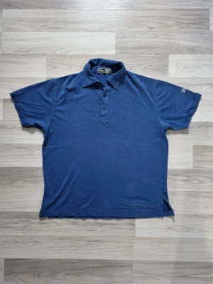 Blå pikétröja från Oscar Jacobson  - Klassisk blå pikétröja från Oscar Jacobson med krage och tre knappar framtill. Tillverkad i mjukt bomullsmaterial och har korta ärmar. Diskret logga broderad på ena ärmen. Perfekt för en avslappnad och stilren look.