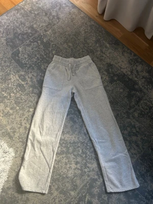 Grå mjukisbyxor med raka ben - Säljer ett par ljusgrå mjukisbyxor med raka ben och resår i midjan. Byxorna stora fickor fram samt bakfickor.