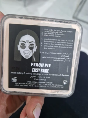 Huda Beauty Easy Bake Peach Pie puder - Löspuder i nyansen Peach Pie från Huda Beauty. Perfekt för baking och att fixera din foundation. Kommer i en fyrkantig plastburk med svart lock och rosa text. Ger en matt finish och jämnar ut hudtonen.
