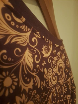 Lila t-shirt medmönster - Snygg lila t-shirt med korta ärmar och ett detaljerat blommigt mönster i beige. Perfekt för dig som vill sticka ut med en unik och färgglad stil. T-shirten har en klassisk passform och rund halsringning.