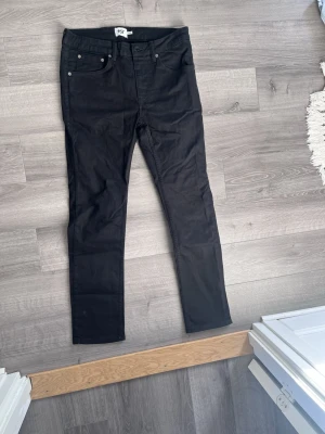 Svarta raka jeans från 157 - Svarta jeans från 157 med klassisk femficksdesign och raka ben. Jeansen har normal midja och stängs med dragkedja och knapp. Perfekta för en clean och stilren look. Materialet är bomull med lite stretch för extra komfort.