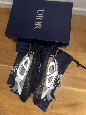 Dior B30 sneakers svart/grå - Säljer ett par Dior B30 sneakers i svart, vitt och grått med chunky sula och stora CD-detaljer på sidan. Skorna har meshpaneler och läderdetaljer för en lyxig och sportig look. Levereras med originalkartong och dustbag.