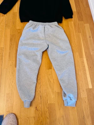 Grå mjukisbyxor och tröja med fleecefoder - Mysiga grå mjukisbyxor med elastisk midja och muddar vid bensluten. Insidan är fodrad med mjuk, gul fleece som gör dem extra varma och sköna. Svart fleece tröja. Perfekta för chill dagar hemma eller när du vill ta en promenad i det kalla vädret Mjukisbyxor och tröja som är fodrade. Storlek L Perfekta för kalla vinterdagar Knappt använda 