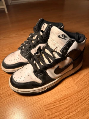 Nike Dunk High svartvita sneakers - Nike Dunk High sneakers i svart och vitt läder med klassisk Swoosh-logga på sidan. Högt skaft, svarta skosnören och perforerad tåbox för extra ventilation. Tidlös och clean design som passar till många olika stilar.