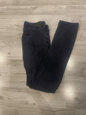 Mörkblå Lee jeans - Snygga mörkblå jeans från Lee med klassisk femficksdesign och raka ben. Jeansen har en diskret Lee-logga på bakfickan och är tillverkade i ett mjukt denimtyg som ger en skön passform. Perfekta för dig som gillar en stilren och tidlös look.