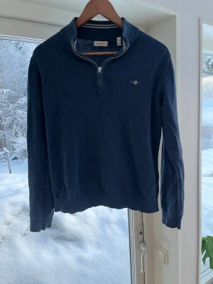 Marinblå halvzip-tröja från GANT - Snygg marinblå tröja från GANT med halv dragkedja och liten broderad logga på bröstet. Tröjan har ribbade muddar vid ärmslut och nederkant samt hög krage. Perfekt för lager-på-lager och klassisk stil.
