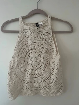 Beige virkad linnetopp från H&M - Säljer en beige virkad linnetopp från H&M med ett snyggt cirkelmönster framtill. Toppen är ärmlös och har en bohemisk känsla, perfekt till sommaren. Materialet är bomull och toppen har en croppad passform.