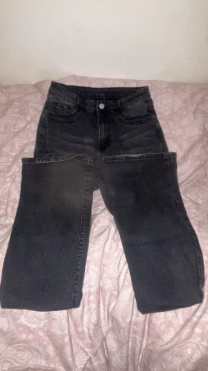 Svarta utsvängda jeans med hög midja - Säljer ett par svarta utsvängda jeans och hög midja. Klassisk femficksmodell med knapp och dragkedja framtill. Jeansen har en stilren look och passar perfekt till en avslappnad vardagsstil. Är 1,70cm lång och passar bra i längden bara att dom var lite för stora på mig vid midjan.