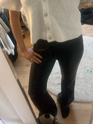 Svarta skinbyxor - Säljer ett par svarta bootcut byxor med medellåg midja. Byxorna har en klassisk passform och är tillverkade i mjukt material. Perfekta för dig som gillar en tidlös och clean look.