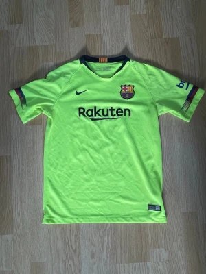 FC Barcelona Nike t-shirt  - Säljer en neongul FC Barcelona t-shirt från Nike med Rakuten-tryck på bröstet och klubbmärke. Tillverkad i polyester med Dri-FIT-teknologi. Perfekt till sommaren, eller om du bara ska se fet ut på idrotten i skolan. Den sitter som S, trots att det står att den är XL.