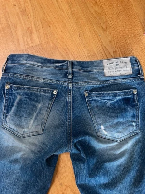 Blå bootcut jeans från Chocoholic - Snygga blå vintage bootcut jeans från Chocoholic med slitningar och tvättade detaljer. Jeansen har två bakfickor med nitar och en klassisk patch bak i midjan. Tillverkade i denim med en cool vintage look och raka ben. Sitter perfekt på mig som vanligtvis har storlek 36