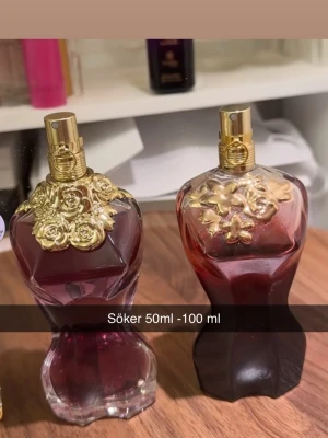 Parfymflaskor med gulddetaljer - Två eleganta parfymflaskor i form av kvinnokroppar, tillverkade i glas med mörkröd färg. Flaskorna har lyxiga guldfärgade blommönster på toppen och guldfärgade spraymunstycken. Perfekt för dig som gillar unika och dekorativa parfymflaskor.