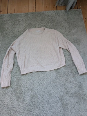 Beige ribbstickad tröja - Säljer en beige ribbstickad tröja med rund hals och långa ärmar. Tröjan har en avslappnad passform och är tillverkad i ett mjukt material som passar perfekt till jeans eller kjol.