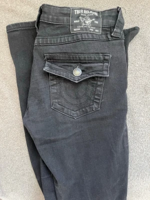 Svarta True Religion jeans bootcut - Säljer ett par svarta jeans från True Religion. Modellen har bootcut-ben och låg midja. Storlek 27 så skulle säga M, har stretchigt material. Svarta men lite urtvättade och bra skick i övrigt 