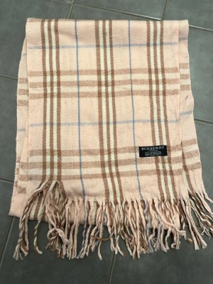 Burberry halsduk - Säljer en riktigt schysst burberry halsduk i beige/ rosa klassisk färg. Priset är ej hugget i sten! Tveka inte att skriva vid frågor/funderingar🤩🤝