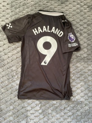 Manchester City Haaland tröja Puma M - Säljer en svart Manchester City matchtröja med Haaland och nummer 9 på ryggen. Tröjan har vita detaljer, klubbmärke på bröstet, Premier League-märke på ärmen och Etihad Airways-tryck framtill. Tillverkad i polyester och har klassisk krage.